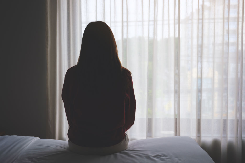 Femme assise sur un lit, dos tourné